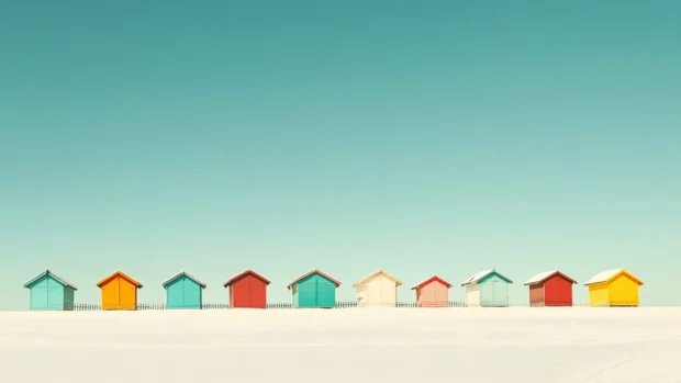 A line of colorful beach huts stands proudly against a cloudless sky.