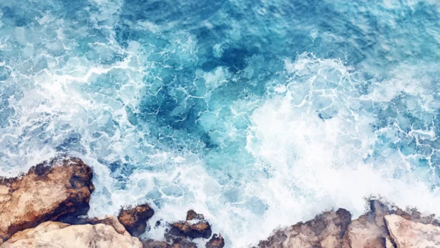 A rocky shoreline kissed by watercolor ocean foam.