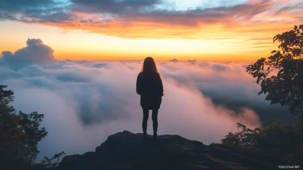 A silhouette of a girl standing on a mountaintop, watching the sunrise in a breathtaking view.