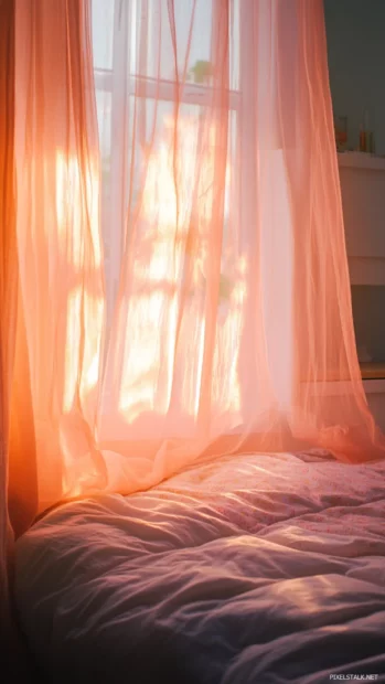 A warm light passing through sheer pink curtains onto a bed.