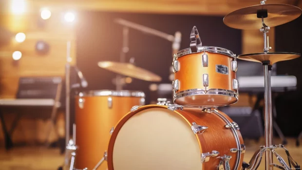 An artistic view of a drum kit in the corner of a well lit studio, with instruments and recording gear arranged around it, creating an energetic and inspiring atmosphere.
