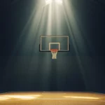 Basketball bouncing under spotlight on moody indoor court.
