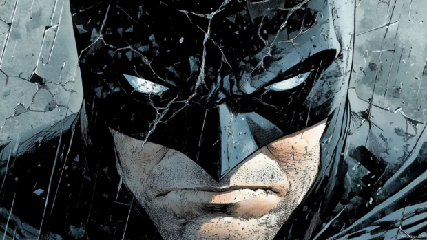 Close up of Batmans face under a cracked mask shadows covering.