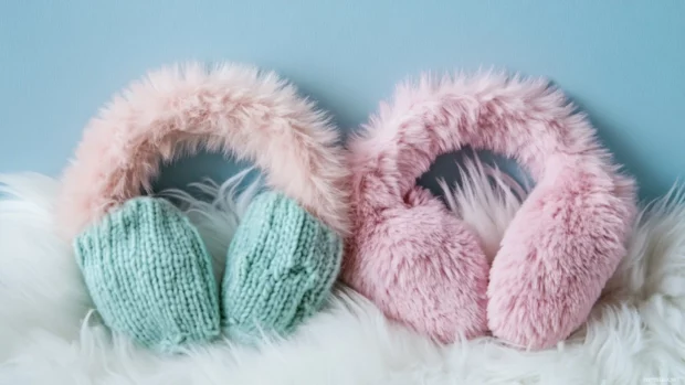 Fluffy pink earmuffs beside mint colored mittens.