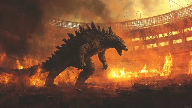Godzilla lunging forward with flames in the background of a ruined stadium.