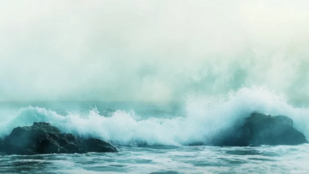 Misty watercolor ocean waves breaking gently on coastal rocks.