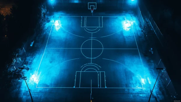 Night basketball court lit by moody blue LED lights and shadows.