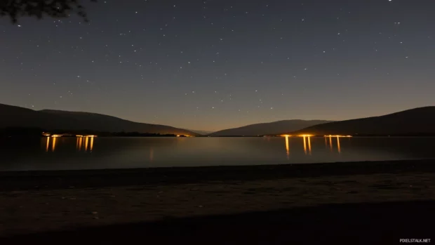 Peaceful and enchanting atmosphere created by a serene night scene with a vibrant starry sky perfectly reflected on the water surface of a calm lake.