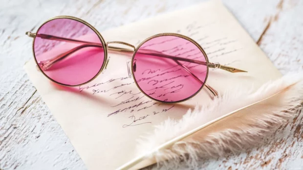 Pink sunglasses placed beside a love letter and feather pen.