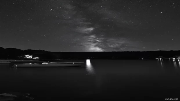 Serene night scene showcasing vibrant starry sky above calm lake where the stars reflect perfectly on water surface creating peaceful and enchanting atmosphere.