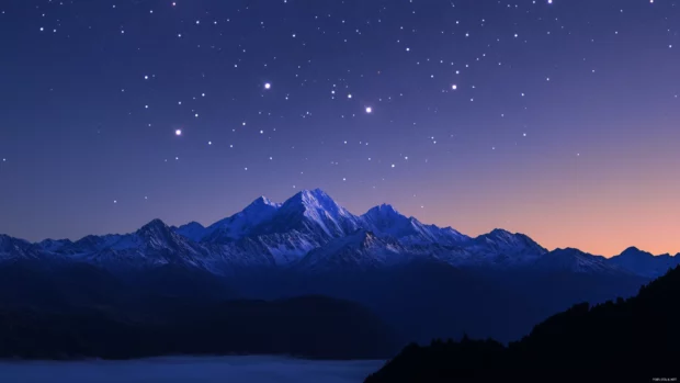 Silent peaks crowned by distant starfire, becoming a canvas for beautiful stars wallpaper for desktop.