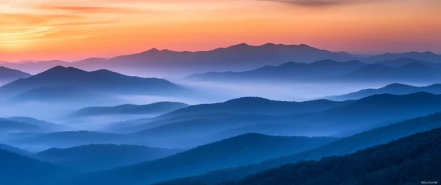 A breathtaking mountain landscape at 3440x1440 resolution where misty peaks meet a glowing dawn sky.