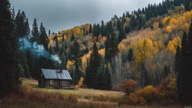 A cozy wooden cabin nestled among Beautiful Fall trees with smoke rising gently from the chimney.