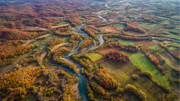 An aerial perspective of a sprawling fall landscape where rivers, forests, and fields blend into a patchwork of autumn beauty.