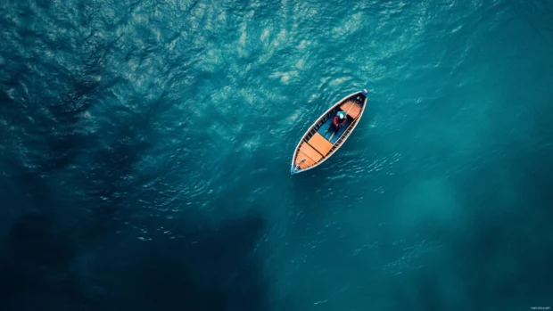 An aerial view of a fisherman in a tiny boat surrounded by deep blue water.