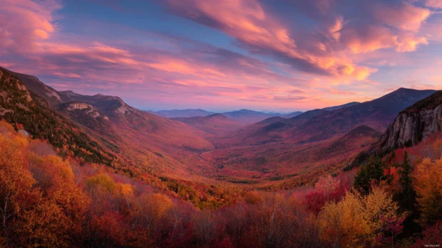 Fall MacBook Pro wallpaper capturing panoramic mountain valley ablaze in fiery foliage under pastel sky.