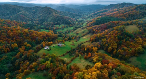 Fall foliage 4K wallpaper presenting aerial view of rolling hills ablaze with multicolored autumn woods.