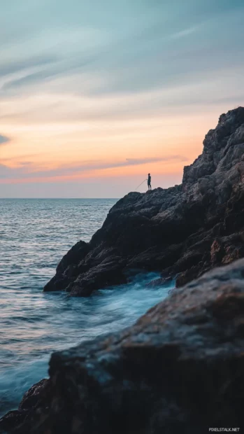 Fishing moment captured near a rocky shore with soft waves and pastel skies.