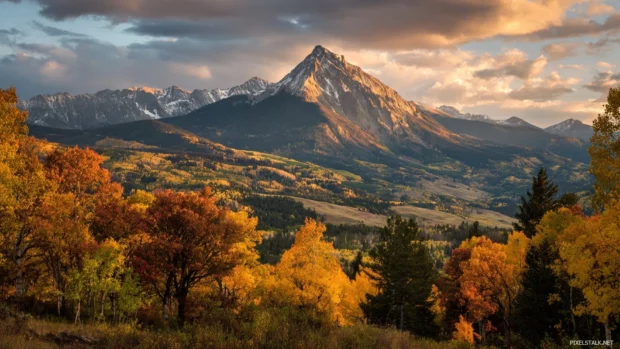 Majestic mountains in the distance glowing under the golden light of Beautiful Fall with colorful trees in the foreground.