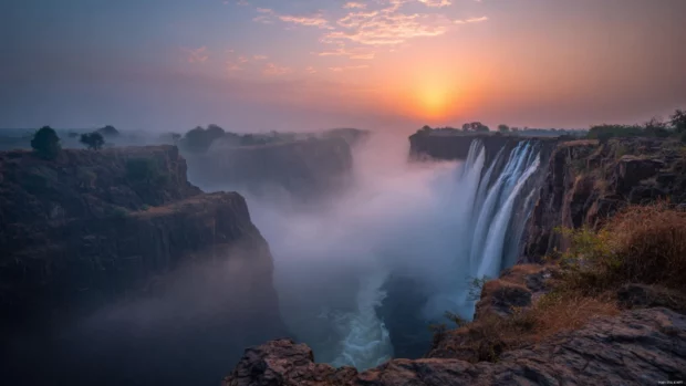 Mystical fog rolling over a grand Waterfall at sunrise creating a dreamy atmosphere.