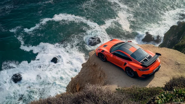 Porsche 911 gt3 rs parked dramatically on a coastal cliff with waves crashing below.