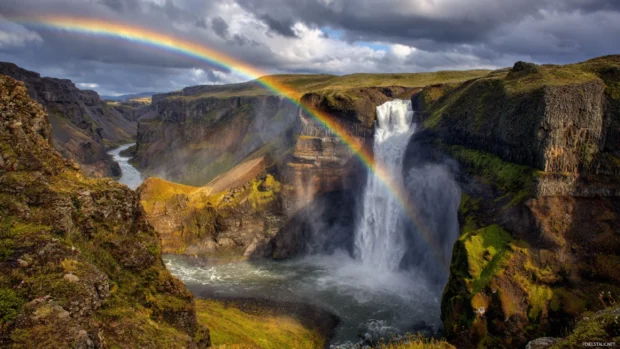 Rainbow waterfall desktop wallpaper depicting powerful waterfall with arching rainbow bridge created by sunlit spray over dramatic cliffs.