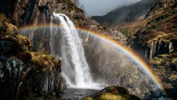 Waterfall cascading down mossy cliffs with a vibrant rainbow arching across the mist (2).