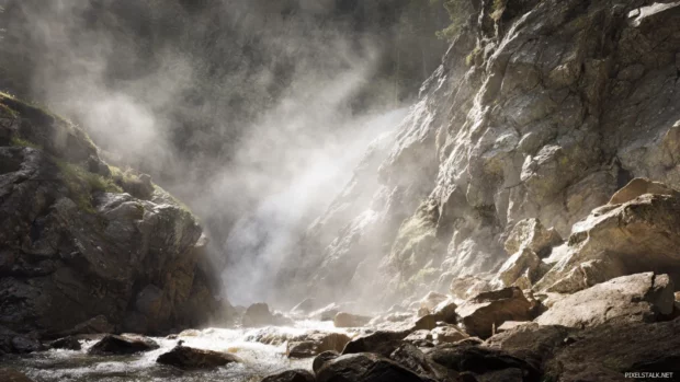 Waterfall crashing down into rocky terrain with mist creating magical light patterns.