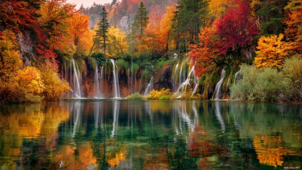 Waterfall desktop wallpaper depicting multiple tiered falls amid vibrant autumn forest reflected on calm lake.