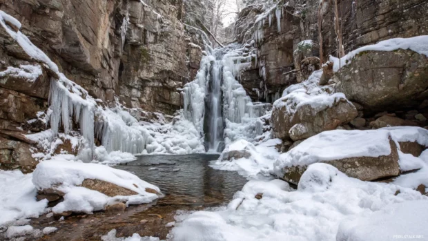 Waterfall in winter partially frozen with shimmering icicles and snow covered rocks.