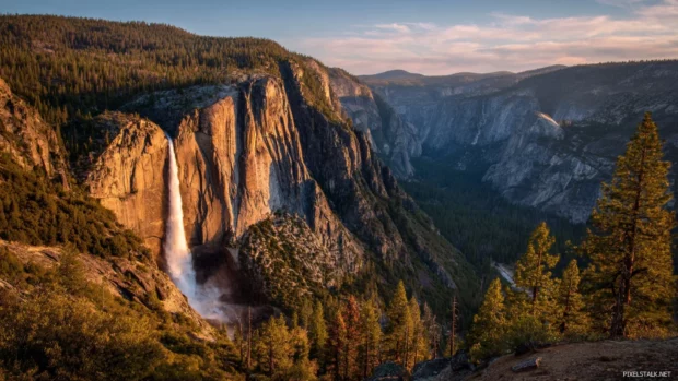 Waterfall landscape wallpaper showing majestic falls at golden hour with rainbow mist rising above pool.