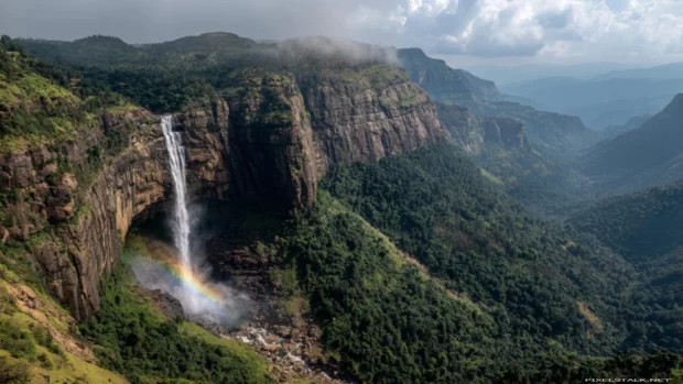 Waterfall pouring from rugged cliffs with a soft rainbow curving through the rising mist (2).