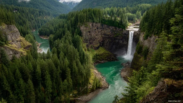 Waterfall pouring from tall cliffs into an emerald river winding through a green canyon.