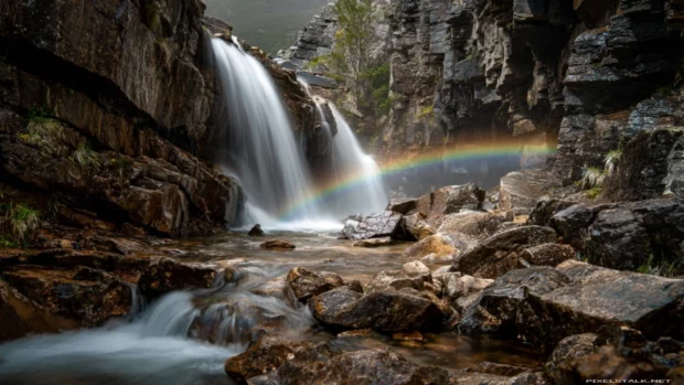 Waterfall tumbling over layered rocks while a delicate rainbow curves above the foamy water (2).
