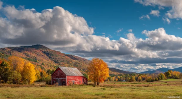 A scenic Fall landscape in Vermont featuring a red barn, golden foliage and a calm blue sky.