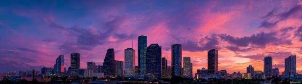 A vibrant city skyline at dusk with colorful lights illuminating three monitors in a seamless panorama.