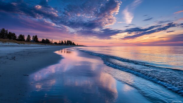 Amazing backgrounds for PC, A tranquil beach scene at sunset with soft waves lapping at the shore and colorful clouds reflecting on the water.