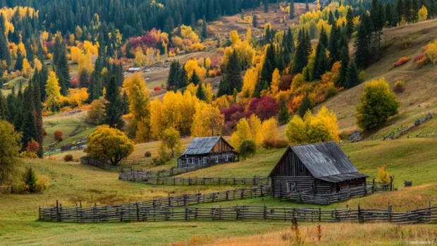 Autumn colors explode across the countryside, with rustic barns and wooden fences nestled in a scenic landscape.