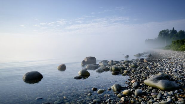 Beach images backgrounds, An early morning beach with mist rising from the water and smooth stones lining the shore.