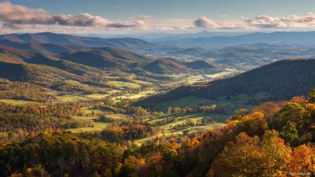 Bright Fall landscape featuring mountain ridges, a patchwork of forests and sunlit fields stretching to the horizon.