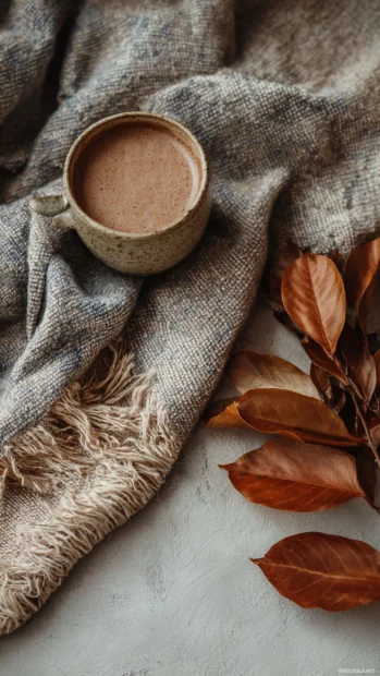 Cozy Autumn flatlay with a cup of hot chocolate, dried leaves, and a wool scarf in gentle Aesthetic colors.