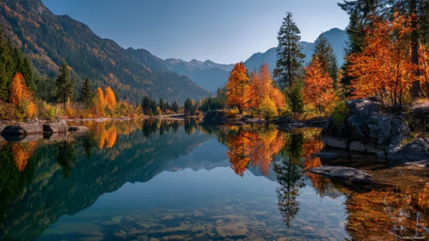 Fall reflections on a serene mountain lake with orange and red trees mirrored in the crystal clear water.