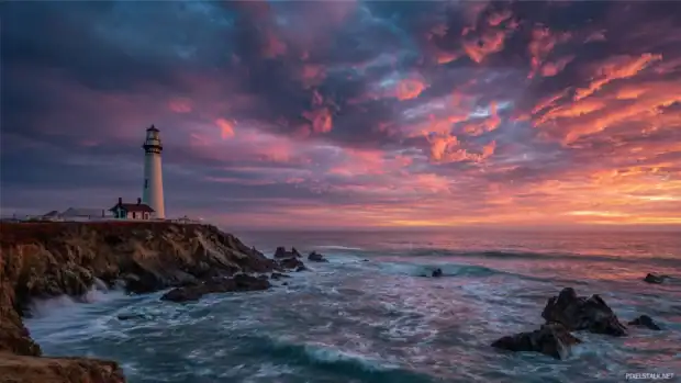 Lighthouse standing tall on a rocky cliff surrounded by crashing waves under a dramatic sunset sky.