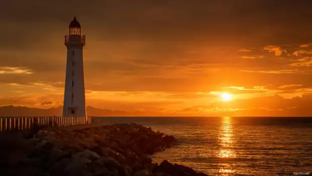 Lighthouse sunset desktop wallpaper showcasing golden sunset casting warm light on coastal tower and sea horizon.