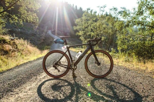 A 3T bike is parked on a gravel road surrounded by trees with sunlight streaming through, HD Desktop Wallpaper