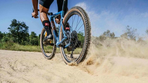 A cyclist is riding a 3T bike on a sandy path creating dust clouds while moving fast, HD Desktop Wallpaper