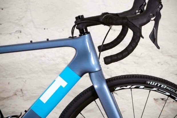 A close up of a 3T bike with blue frame and black handlebars against a white textured wall, 2K Desktop Wallpaper