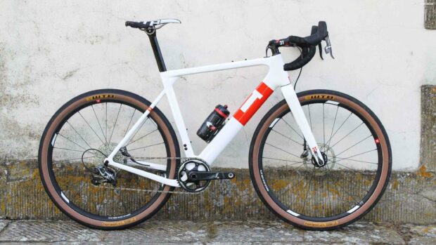 A white 3T bike with red accents stands against a textured wall, 2K Desktop Wallpaper