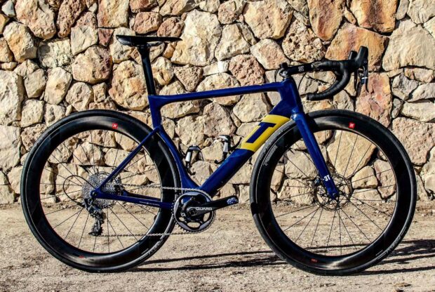A sleek 3T bike is parked on a dirt surface with a textured stone wall in the background, HD Desktop Wallpaper