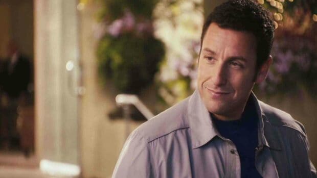 Adam Sandler is smiling gently while wearing a light jacket in an outdoor setting, HD Desktop Wallpaper